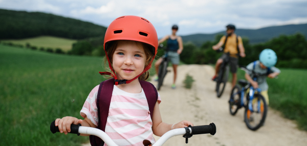 A portrait of excited little girl with his family at backround riding bike on path in park in summer