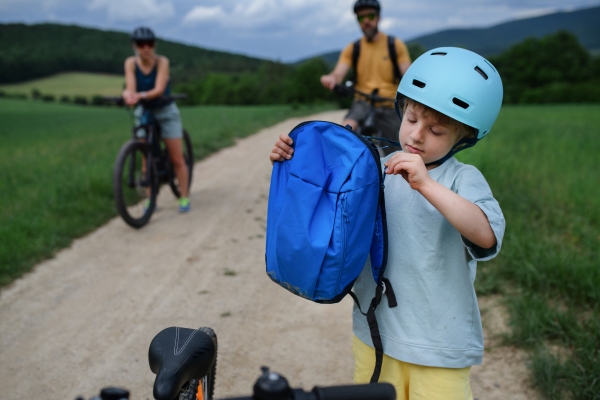 A young family with little child riding bicycles on road in village in summer.