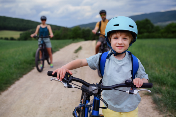 A young family with little child riding bicycles on road in village in summer.