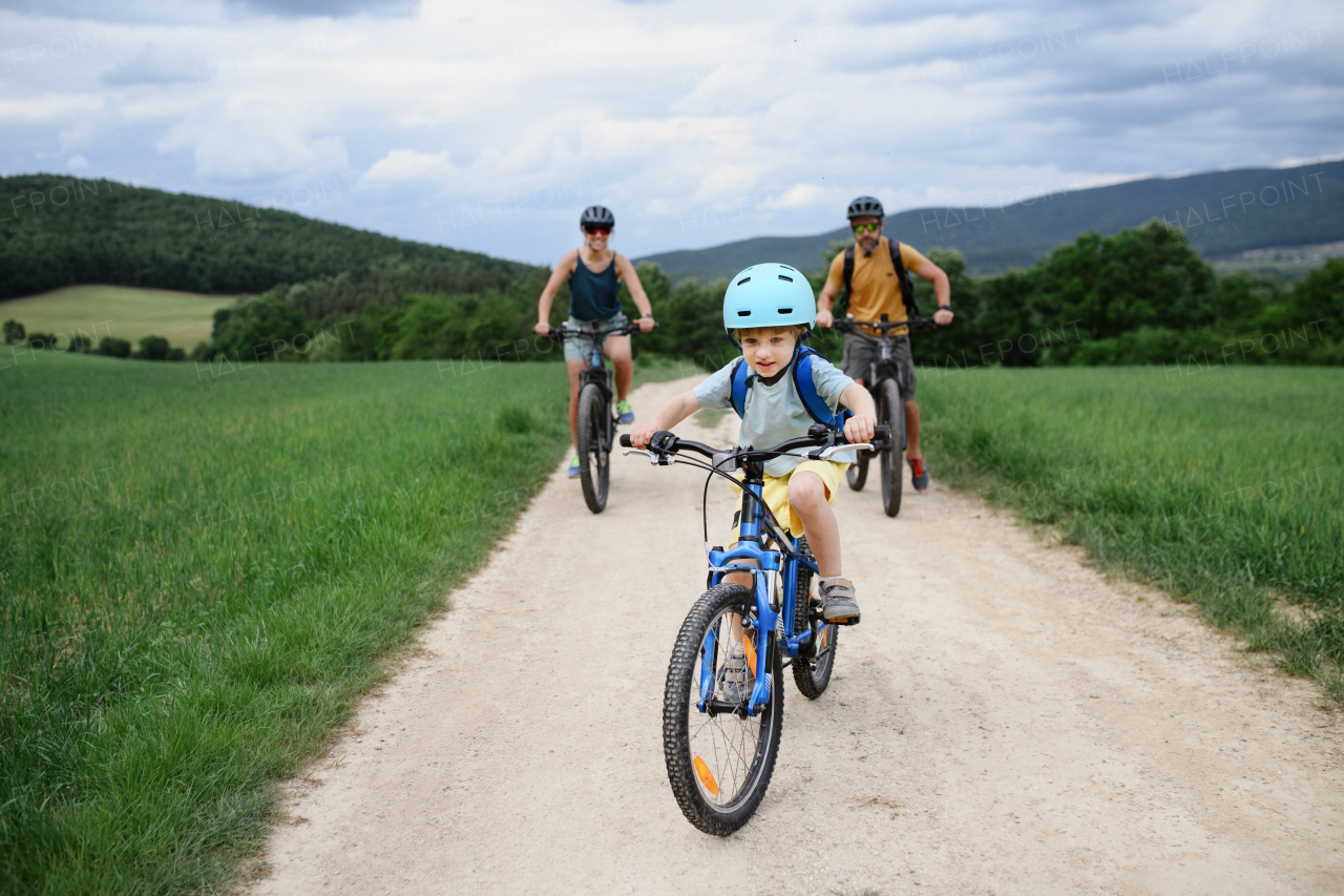 A portrait of excited little boy with his parents at backround riding bike on path in park in summer