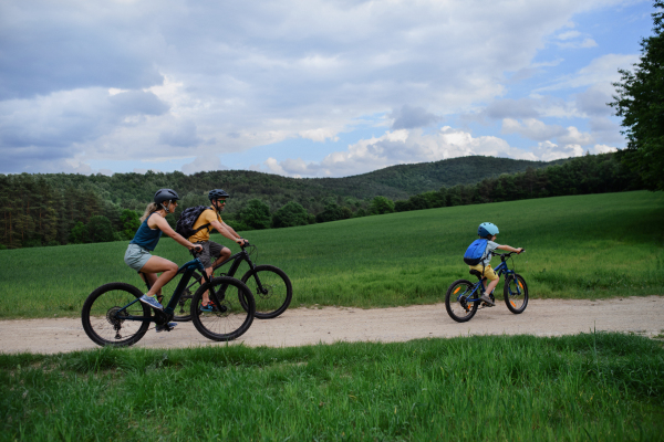 A young family with little child riding bicycles on road in village in summer.