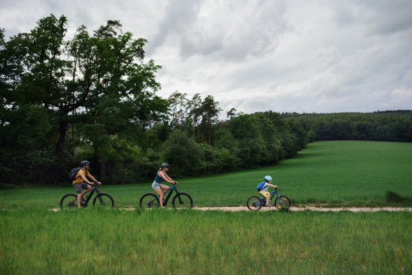 A young family with little child riding bicycles on path in park in summer. Side view.