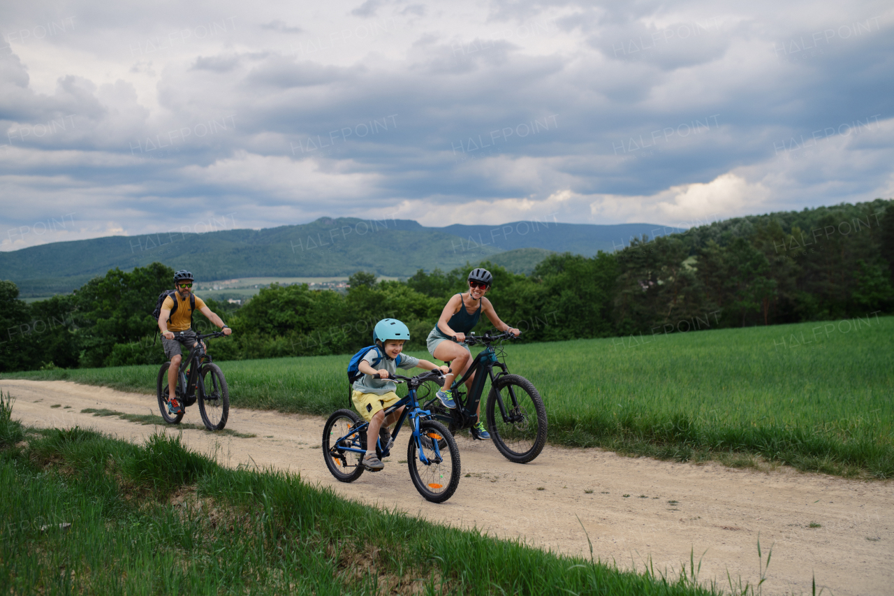 A young family with little child riding bicycles on road in village in summer.