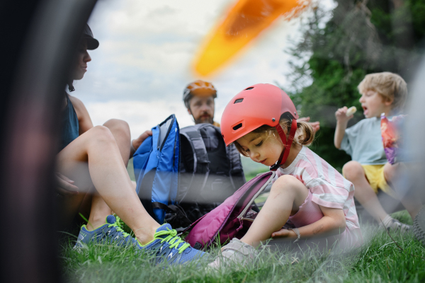 A young family with little children resting after bike ride, sitting on grass in park in summer.