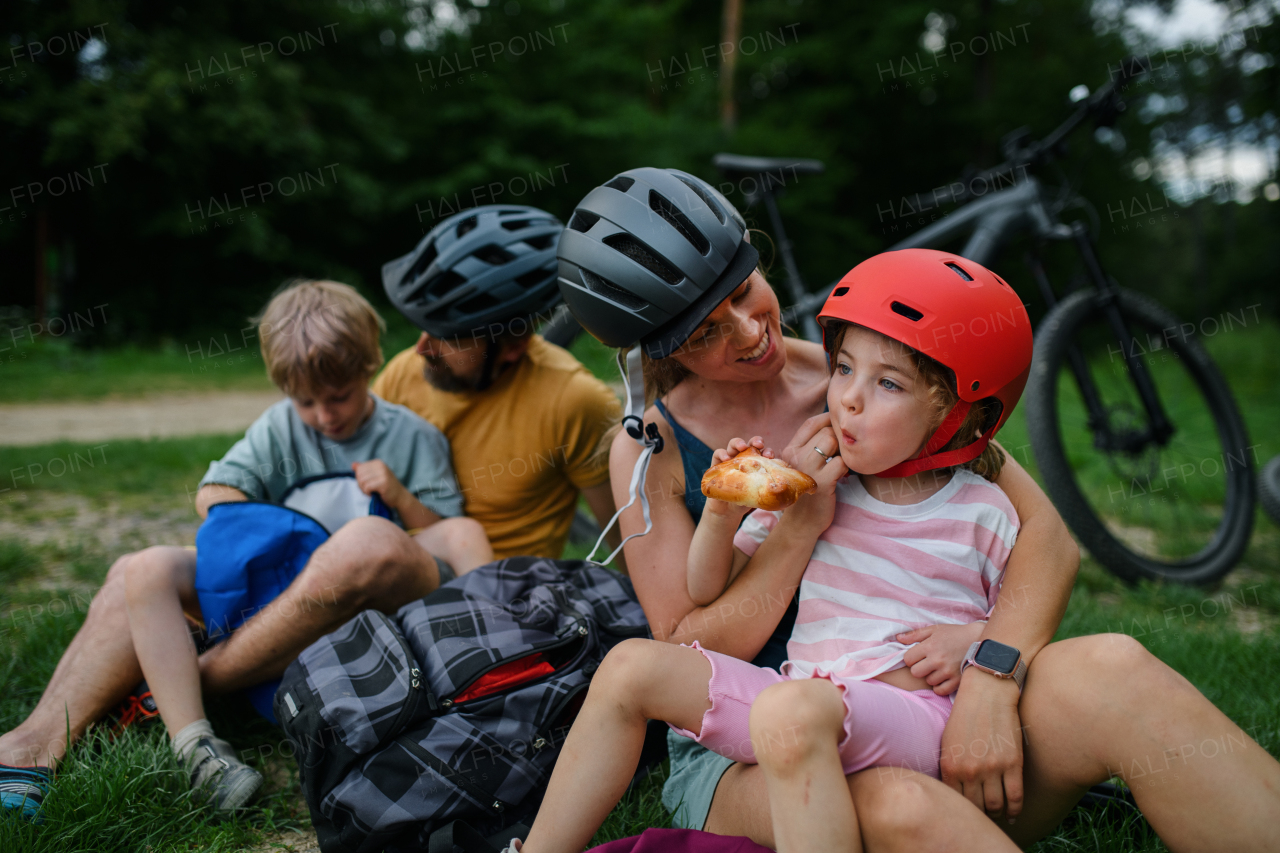 A young family with little children resting after bike ride, sitting on grass in park in summer.