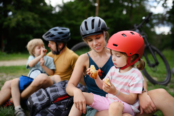 A young family with little children resting after bike ride, sitting on grass in park in summer.