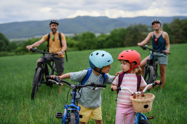 A portrait of young family with little children preapring for bike ride, standing with bicycles in nature.