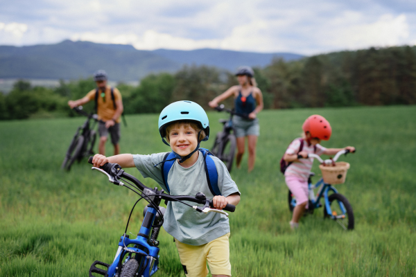 A portrait of young family with little children preapring for bike ride, standing with bicycles in nature.