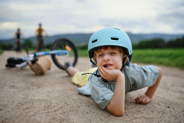 A little boy fell off his bike and lying on path and crying, with his parents coming to help him.