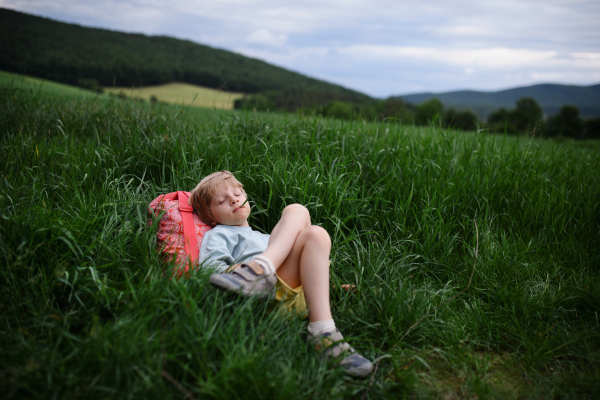 A happy first day of school. Tired schoolboy with backpack, lies on the grass.