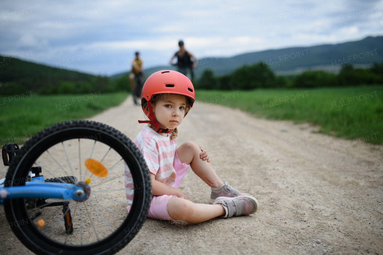 A mother and father rushing to help their little daughter after falling off bicycle outdoors