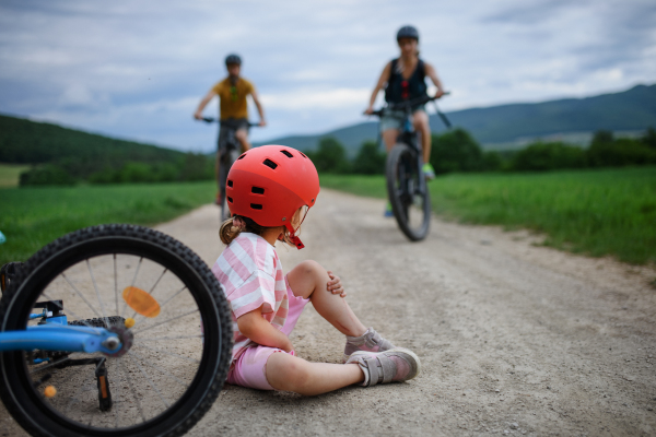 A mother and father rushing to help their little daughter after falling off bicycle outdoors