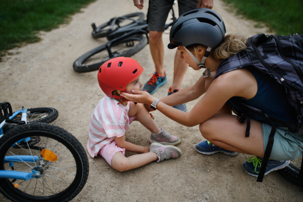 A mother and father helping their little daughter after falling off bicycle outdoors