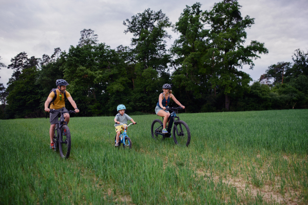 A young family with little child riding bicycles on meadow in village in summer.