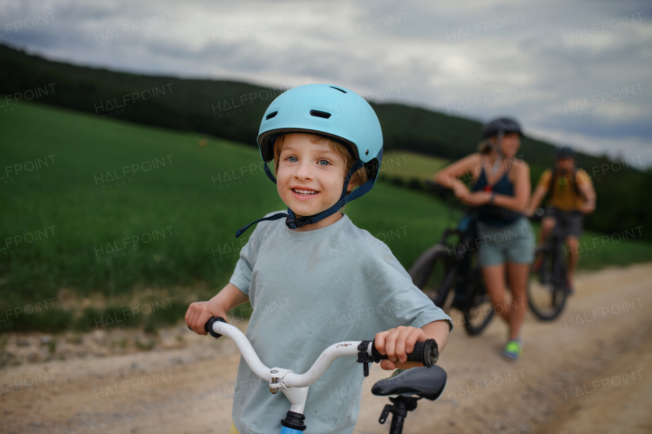 A young family with little child riding bicycles on road in village in summer.