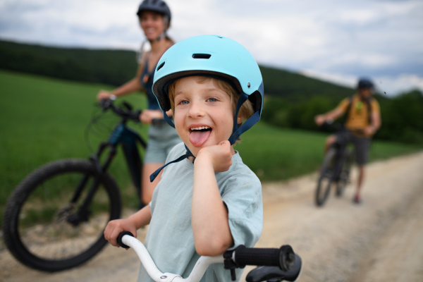 A portrait of excited little boy with his family at backround riding bike on path in park in summer