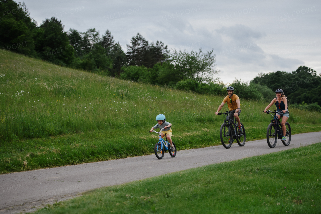 A young family with little child riding bicycles on road in village in summer.