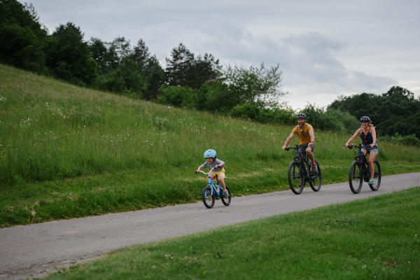 A young family with little child riding bicycles on road in village in summer.