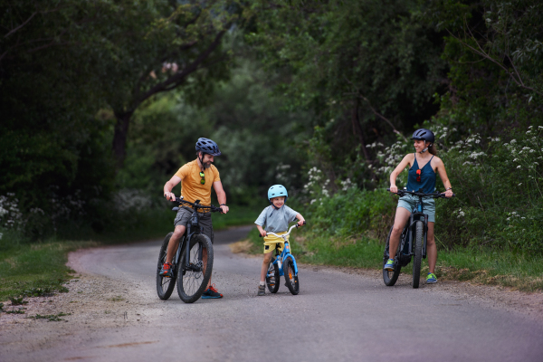 A young family with little child riding bicycles on road in village in summer.