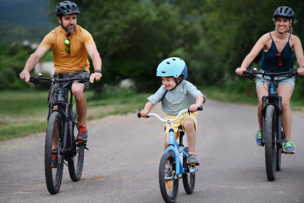 A young family with little child riding bicycles on road in village in summer.