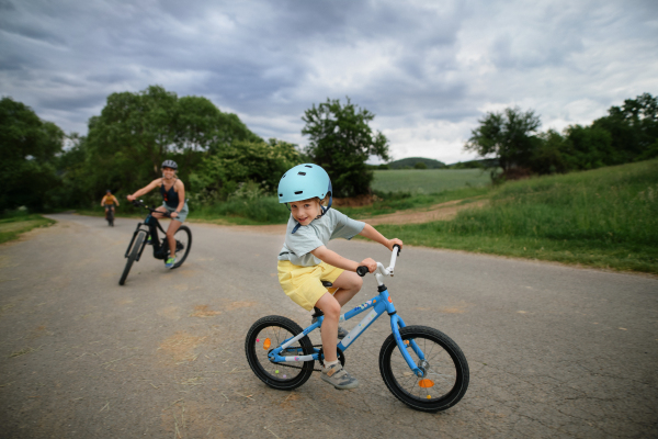 A portrait of excited little boy with his family at backround riding bike on path in park in summer