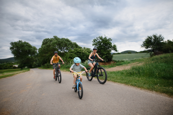 A young family with little child riding bicycles on road in village in summer.