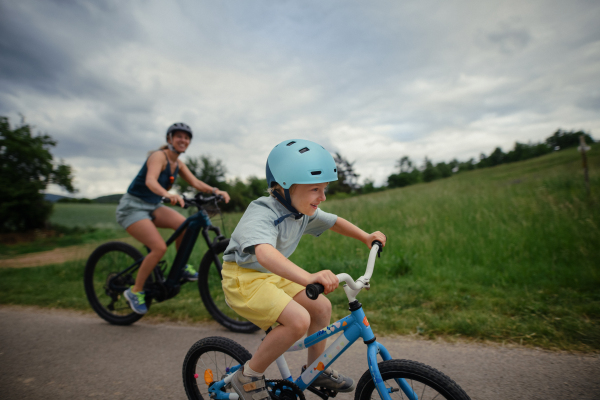 A young family with little child riding bicycles on road in village in summer.