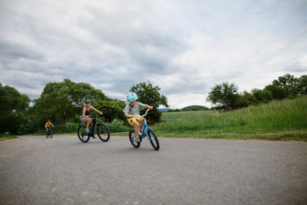 A young family with little child riding bicycles on road in village in summer.