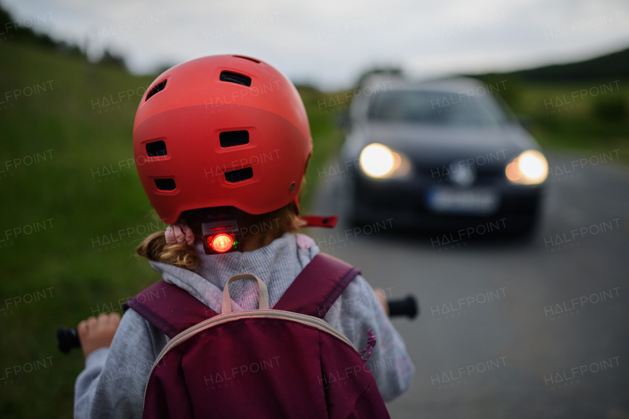 A rear view of child riding bike on road with car in front of her, road safety education concept.