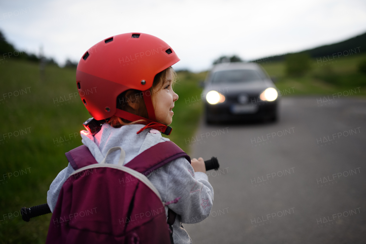 A rear view of child riding bike on road with car in front of her, road safety education concept.