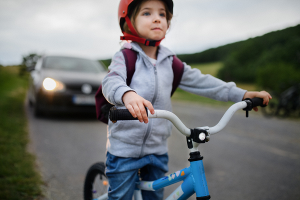 A portrait of excited little girl riding bike on road with car behind her