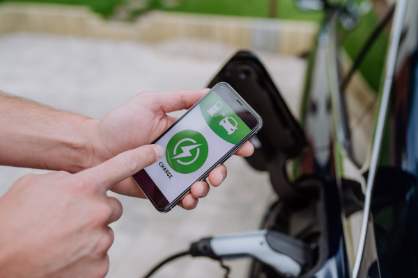 Man setting phone application for charging his electric car at a charging station, closeup.