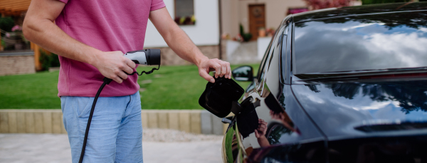 A man holding power supply cable at electric vehicle charging station.