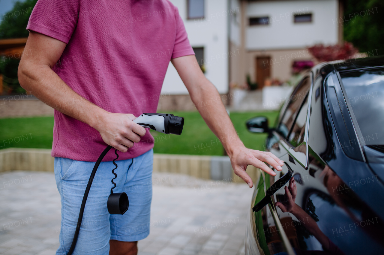 A man holding power supply cable at electric vehicle charging station.