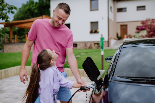 Happy father showing his daughter how to charge their electric car.