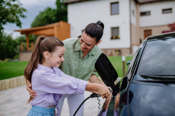 Happy mother showing her daughter how to charge their electric car.