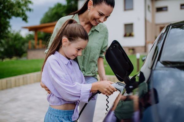 Happy mother showing her daughter how to charge their electric car.