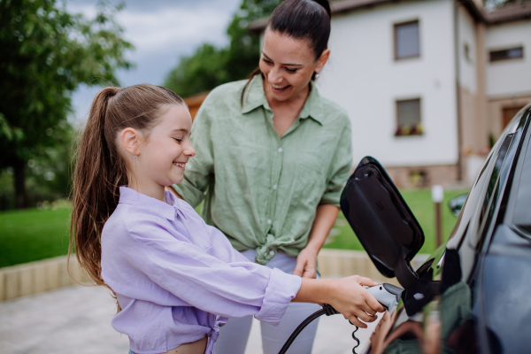 Happy mother showing her daughter how to charge their electric car.