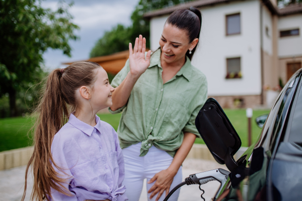 Happy mother showing her daughter how to charge their electric car.