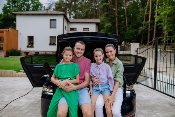 Happy family sitting in a car trunk and waiting for electric car charging.