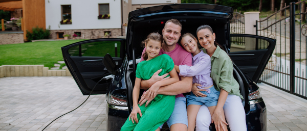 Happy family sitting in a car trunk and waiting for electric car charging.