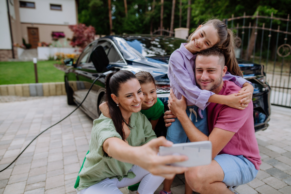 Happy family taking a selfie, waiting for electric car charging.