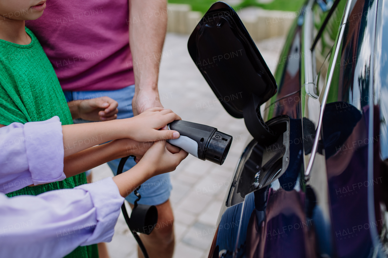 Close-up of father holding power supply cable with his little daughters and charging electric car.