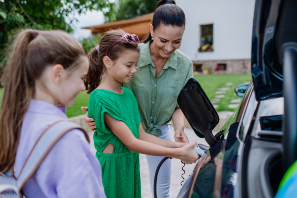 Happy mother showing her daughters how to charge their electric car.