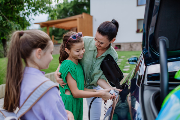 Happy mother showing her daughters how to charge their electric car.