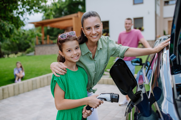 Happy mother showing her daughter how to charge their electric car.