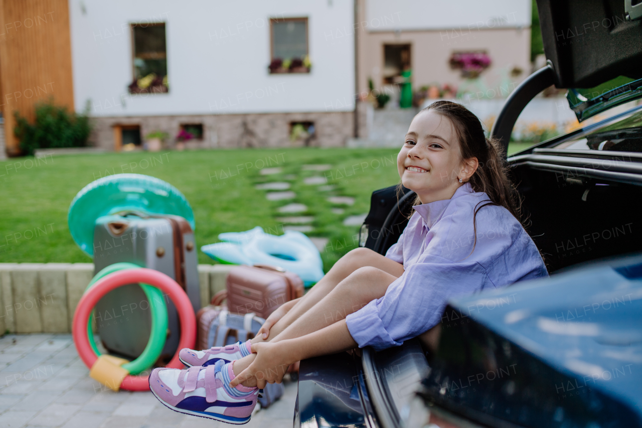 Little girl sitting in car trunk, prepared for a family holiday.