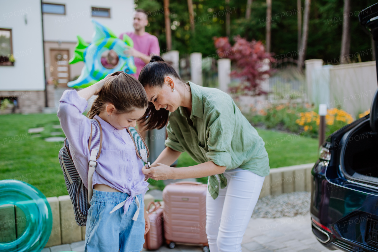 Young family preparing for summer holiday, putting suitcases in a car trunk.