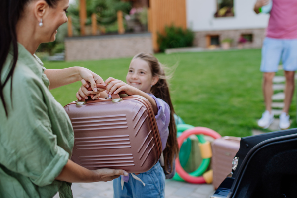 Happy family preparing for a holiday, putting suitcases in a car trunk, while their electric car charging.