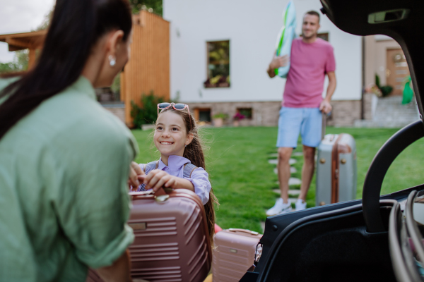 Happy family preparing for a holiday, putting suitcases in a car trunk, while their electric car charging.